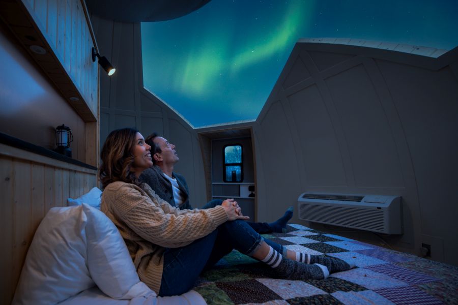 From inside the dome a couple is looking up at the aurora borealis in the night sky.